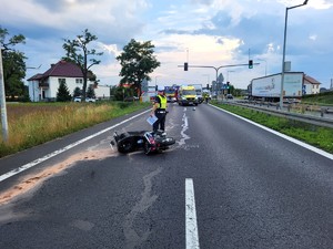 Zdjęcie przedstawia: umundurowanego policjanta i przewrócony motor, leżący na drodze.