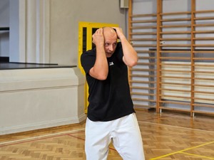 Zdjęcie przedstawia: policjanta zasłaniającego głowę.