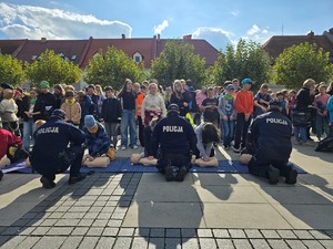 zdjęcie przedstawia: umundurowanych policjantów nadzorujących uczestników wydarzenia podczas reanimacji na manekinach.