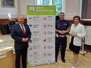 Zdjęcie przestawia policjanta wraz z innym mężczyzną i kobietą podczas uroczystości rozpoczęcia roku szkolnego.