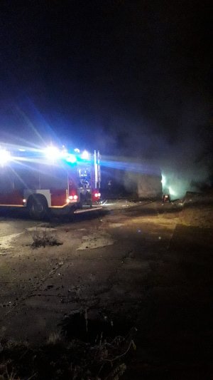 zdjęcie kolorowe, przedstawiające wóz strażacki oraz płonący budynek