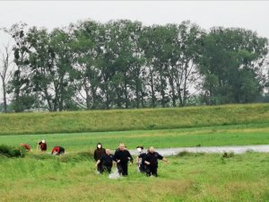 Raciborscy policjanci idą przez wysoką trawę z uratowaną załogą tratwy, a w oddali widać zacumowaną do brzegu tratwę
