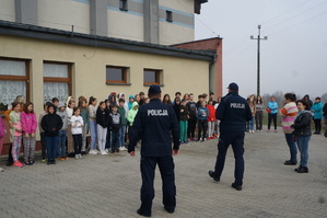 Dzieci i nauczyciele z policjantami na zewnątrz szkoły