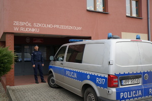 Policjant przy radiowozie przed szkoła w Rudniku