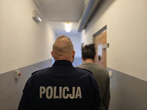 na zdjęciu policjant i zatrzymany mężczyzna stoją tyłem