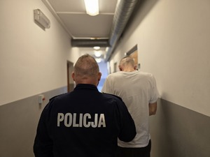 na zdjęciu zatrzymany z policjantem stoją tyłem