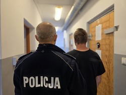 na zdjeciu zatrzymany z policjantem stoja tyłem