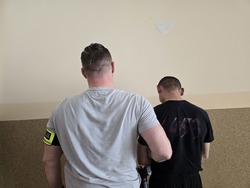 na zdjęciu zatrzymany mężczyzna z policjantem stoją tyłem