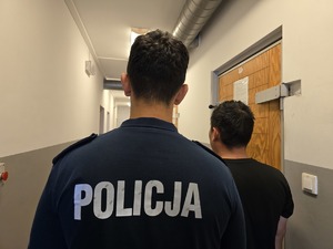 na zdjęciu zatrzymany mężczyzna z policjantem stoja tyłem