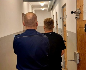 na zdjęciu policjant z zatrzymanym stoją tyłem