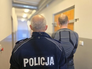 na zdjeciu policjant z zatrzymanym stoja tyłem