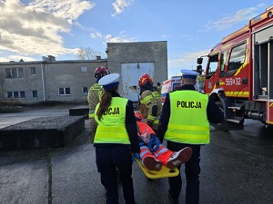na zdjęciu policjanci pomagają nieść poszkodowanego