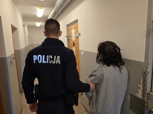 na zdjęciu policjant z zatrzymaną kobieta stoją tyłem