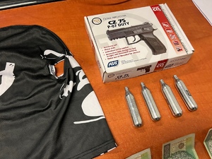zdjęcie w pomieszczeniu biurowym, na biurku leży kominiarka pseudokibiców, banknoty, naboje co2 i pudełko z pistoletem na stalowy śrut z którego strzelali do ofiary