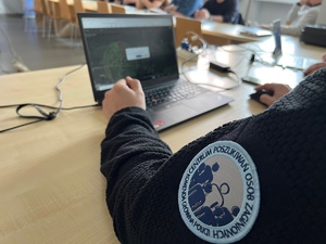 zdjęcie z sali szkoleniowej przestawiające szkolącego z emblematem centrum poszukiwania osób przy laptopie z aplikacją do poszukiwań