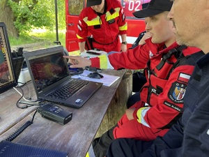 zdjęcie - sztab poszukiwań, strażak pokazuje policjantom aplikację na monitorze komputera