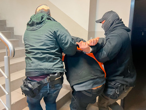 zdjęcie przedstawia policjantów po cywilu prowadzących zatrzymanego korytarzem komendy