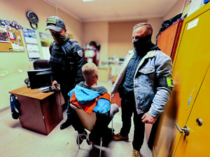 zdjęcie przedstawia policjantów po cywilu stojących przy zatrzymanym w pomieszczeniu biurowym