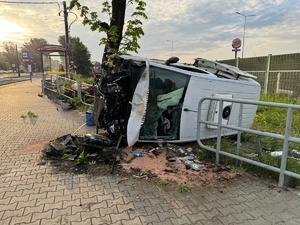 zdjęcie z miejsca zdarzenia - leżący na boku samochód dostawczy, obok drzewo w które uderzył, wiata przystanku tramwajowego i uszkodzone barierki