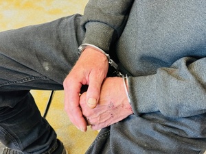 zdjęcie przedstawia zatrzymanego sprawcę siedzącego na krześle z kajdankami na rękach