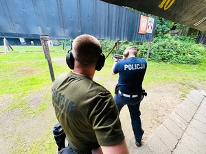 zdjęcie przedstawia zajęcia na strzelnicy otwartej podczas których instruktor kontroluje poprawność strzelania przez policjanta z pistoletu maszynowego