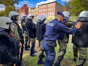 zdjęcie przedstawia szkolenie strażników granicznych - policjant pcha dwóch strażników z szyku do przodu