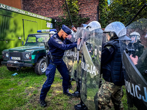 zdjęcie przedstawia szkolenie strażników granicznych - policjant napiera na tarcze kordonu strażników granicznych udając agresywnego migranta