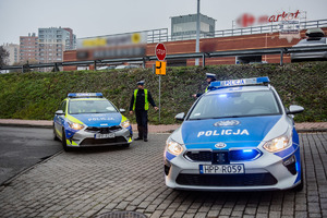 zdjęcie przedstawia dwa policyjne radiowozy blokujące dojazd do centrum handlowego, przy nich policjanci z drogówki