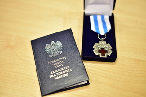 zdjęcie przedstawia odznakę i legitymację honorowego dawcy krwi leżące na stoliku