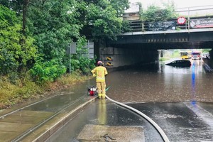 zdjęcie przedstawia zalaną drogę pod wiaduktem kolejowym i strażaka przy pompie