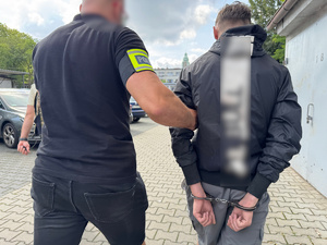zdjęcie przedstawia zatrzymanego prowadzonego przez policjanta