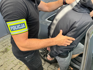 zdjęcie przedstawia zatrzymanego prowadzonego przez policjanta