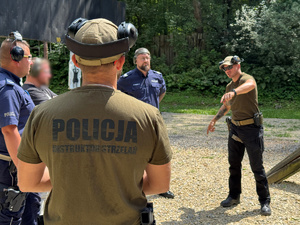 zdjęcie z treningu strzeleckiego pokazuje instruktorów i policjantów na strzelnicy podczas omawiania ćwieczenia