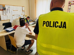 zdjęcie przedstawia policjanta z zatrzymanym kierowcą podczas przesłuchania, drugi policjant stoi za nim