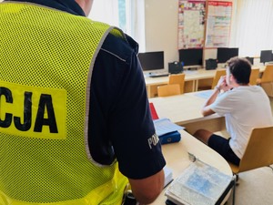 zdjęcie przedstawia policjanta stojącego przy biurku gdzie siedzi zatrzymany