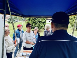 Zdjęcie przedstawia dzielnicowego przy stoisku profilaktycznym oraz uczestników przedsięwzięcia