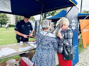 Zdjęcie przedstawia dzielnicowego przy stoisku profilaktycznym oraz uczestników przedsięwzięci