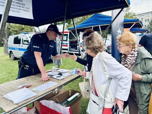 Zdjęcie przedstawia dzielnicowego przy stoisku profilaktycznym oraz uczestników przedsięwzięcia