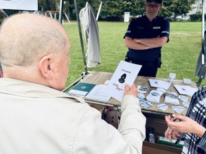 Zdjęcie przedstawia dzielnicowego przy stoisku profilaktycznym oraz uczestników przedsięwzięcia