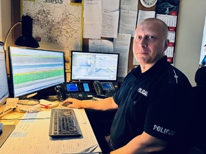 zdjęcie pokazujące zastępcę dyżurnego siedzącego przy swoim stanowisku pracy z komputerami i telefonami