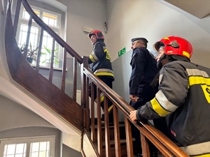 zdjęcie przedstawia strażaków i policjanta na schodach wewnątrz komisariatu