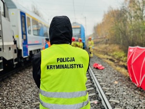 zdjęcie z miejsca wypadku pokazuje pociąg, technika kryminalistyki i pracujących w tle strażaków