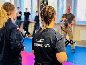 zdjęcie przedstawia uczniów klasy mundurowej z bronią i policyjnego instruktora w trakcie ćwiczeń
