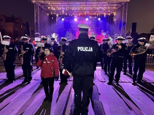 zdjęcie z koncertu policyjnej orkiestry na rudzkim jarmarku - policyjni muzycy grający kolędę i rudzianka śpiewająca ją