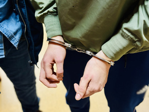 Zdjęcie przedstawia kajdanki na rękach osoby zatrzymanej