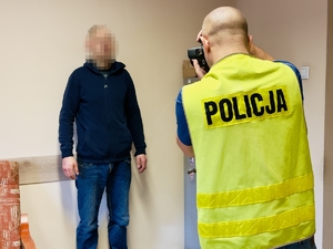 Technik kryminalistyki wykonuje zdjęcia zatrzymanemu mężczyźnie