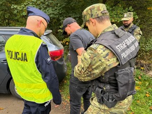 policjant i pogranicznicy przeszukują zatrzymanego mężczyznę