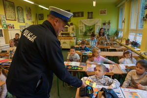 Na zdjęciu policjant ruchu drogowego rozdaje uczniom kamizelki odblaskowe.