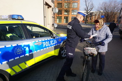 Na zdjęciu oznakowany radiowóz oraz policjant, który rozdaje pieszym odblaski.