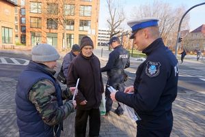 Na zdjęciu policjant podczas akcji dotyczącej bezpieczeństwa pieszych rozdaje odblaski.